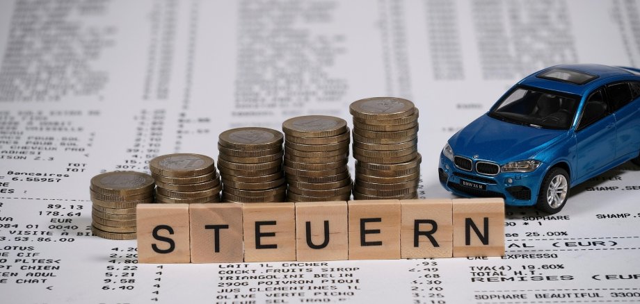Das Bild zeigt mehrere Stapeln von Münzen. Davor steht der Schriftzug Steuern.