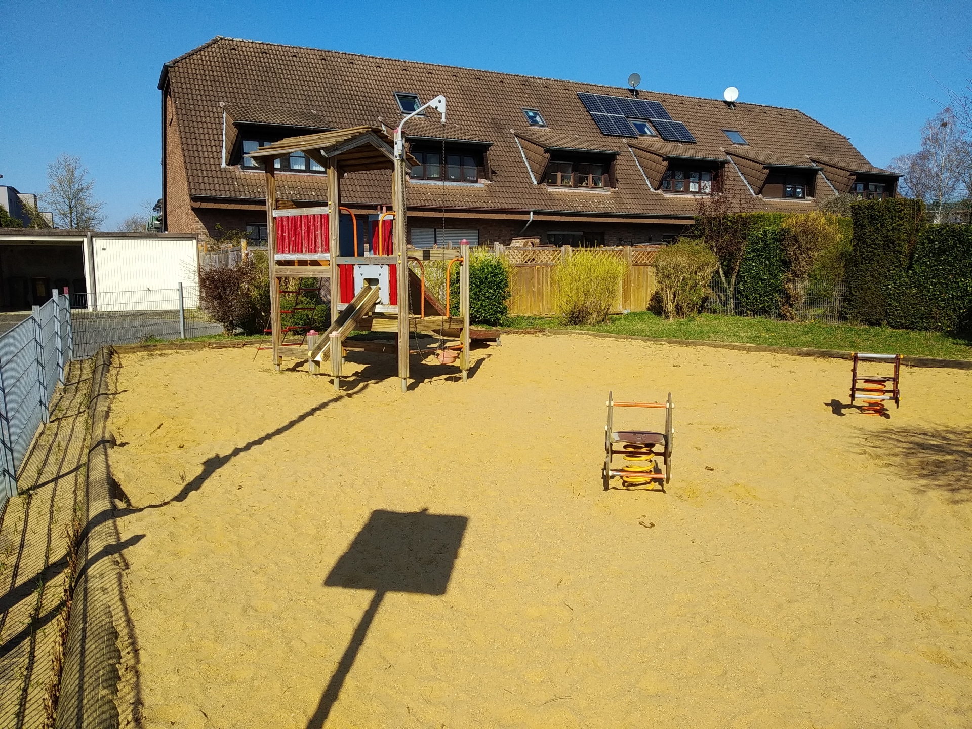 Kinderspielplatz Stuppheide Das Bild zeigt ein Spielhaus mit Rutsche und zwei Federtiere auf einer Sandfläche.