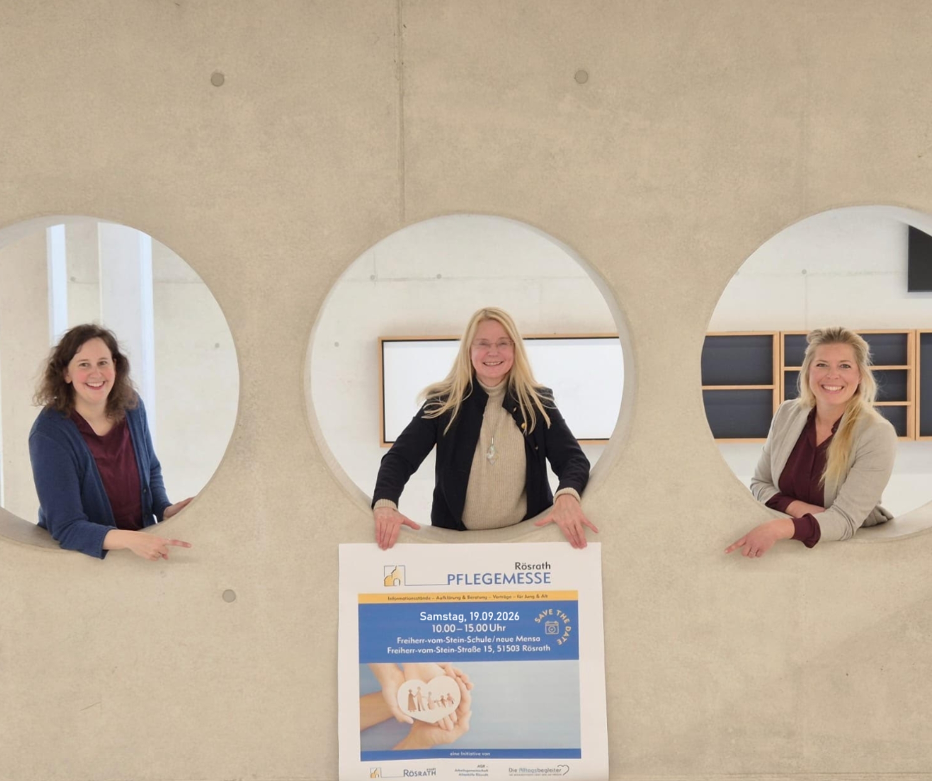 Ankündigung der Rösrather Pflegemesse 2026 Die Organisatorinnen freuen sich auf die Rösrather Pflegemesse 2026 und zeigen auf das entsprechende Veranstaltungsplakat.