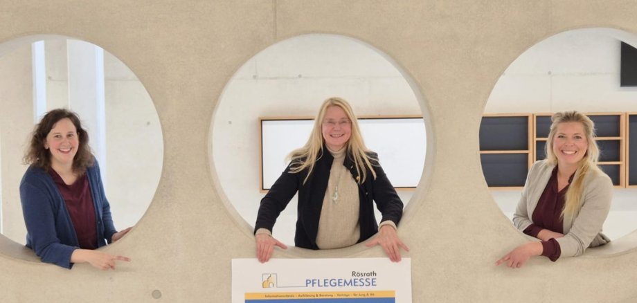 Die Organisatorinnen freuen sich auf die Rösrather Pflegemesse 2026 und zeigen auf das entsprechende Veranstaltungsplakat.