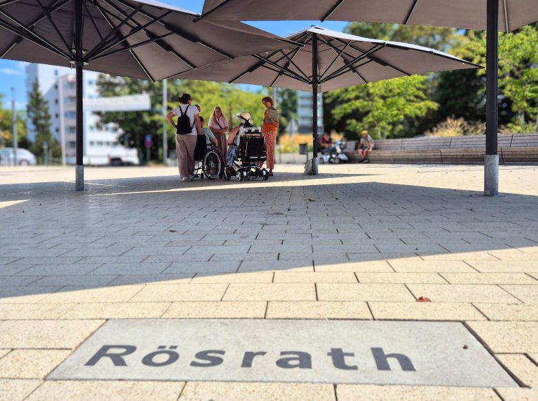 Inklusiver Stadtspaziergang Das Bild zeigt zwei Rollstuhlfahrer mit weiteren Personen beim inklusiven Stadtspaziergang entlang der Hauptstraße in Rösrath-Mitte.