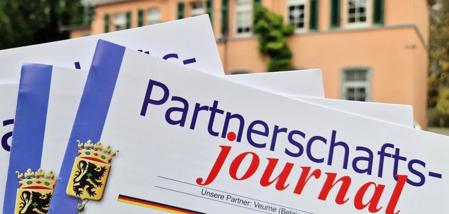 Das Bild zeigt mehrere Exemplare des Partnerschaftsjournal. Im Hintergrund ist das historische Rathaus zu sehen.